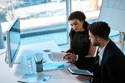 Buy stock photo Cropped shot of two young businesspeople sitting together in the office and using a tablet and paperwork during a discussion