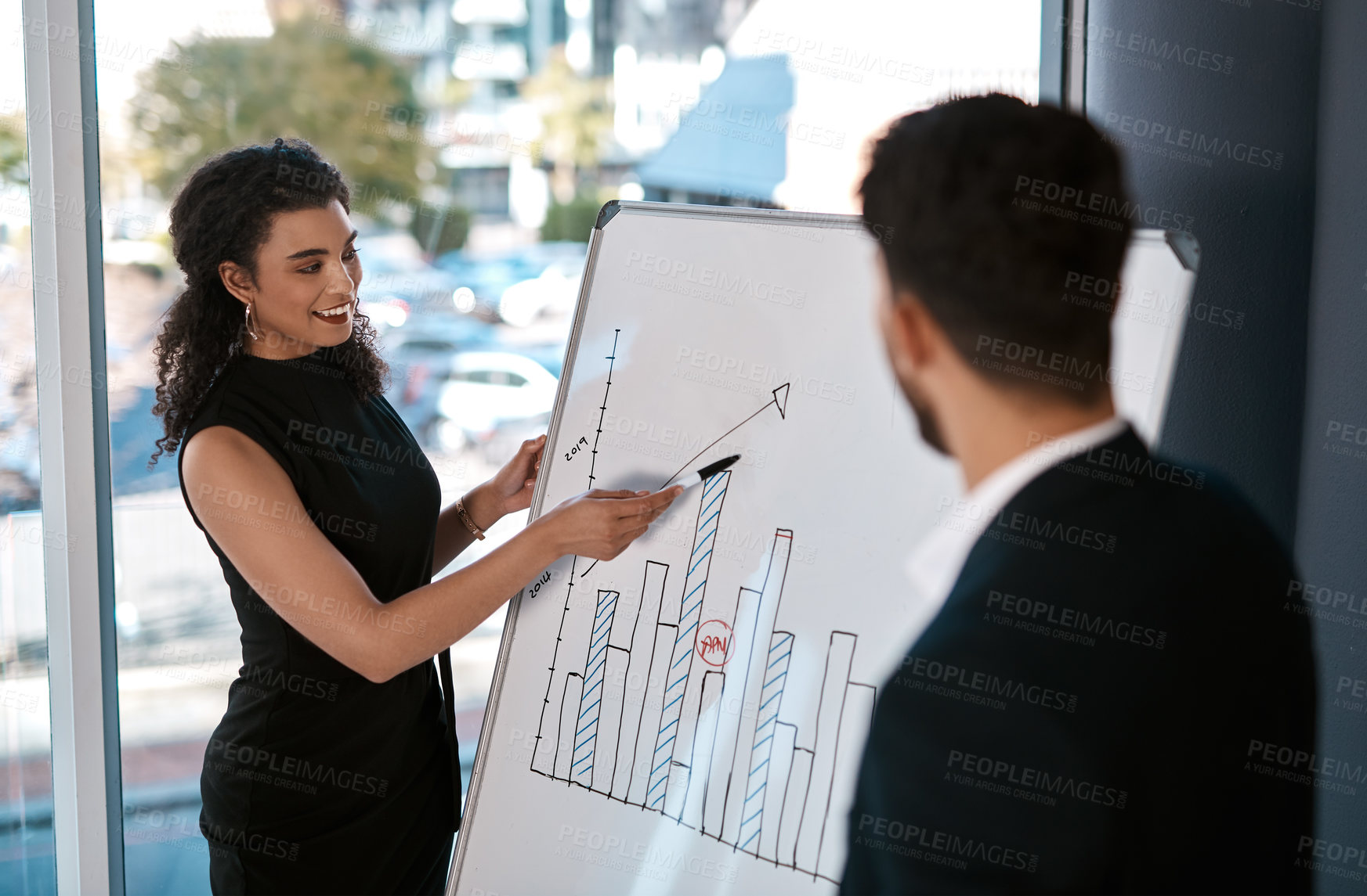 Buy stock photo Cropped shot of an attractive young businesswoman standing and using a white board to present data to her male colleague