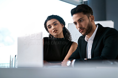 Buy stock photo Cropped shot of two young businesspeople sitting together and having a discussion while using a laptop in the office