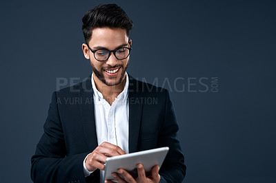 Buy stock photo Cropped shot of a handsome young businessman standing alone and using a tablet against a gray background in the studio