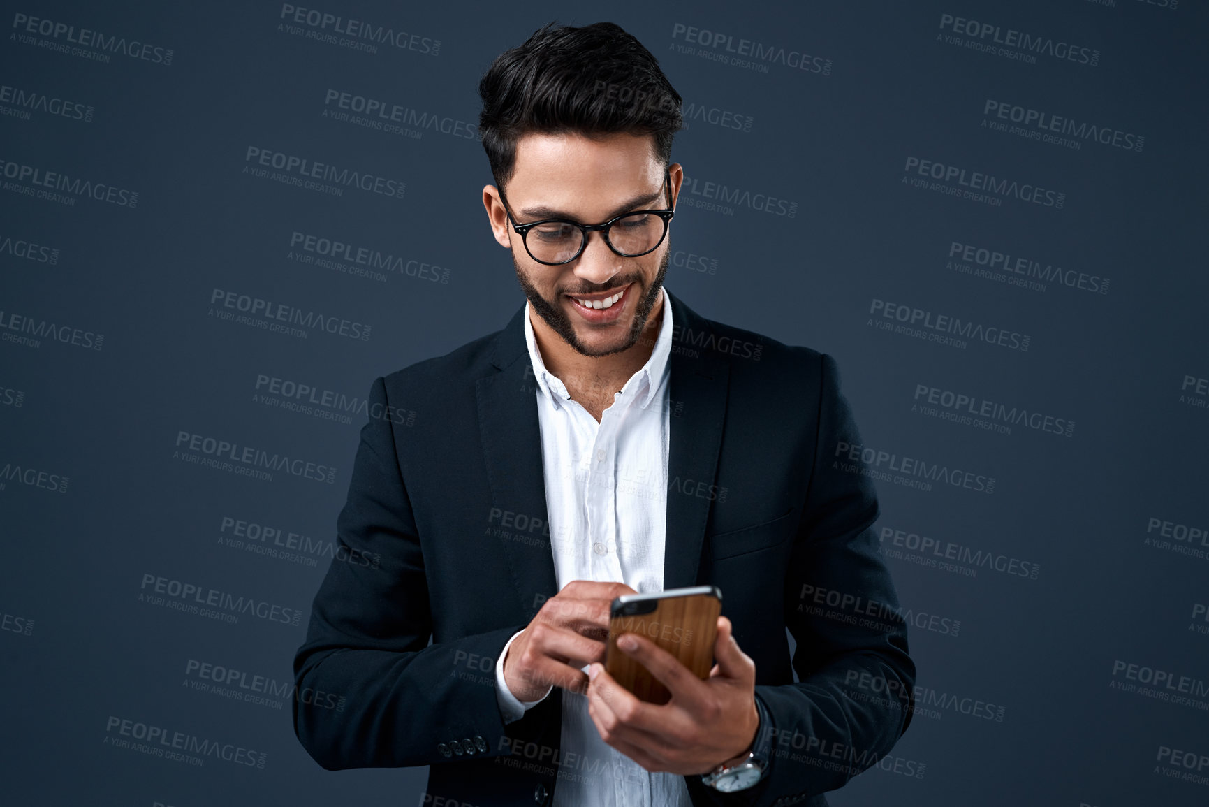 Buy stock photo Cropped shot of a handsome young businessman standing alone against a gray studio background and texting on his cellphone