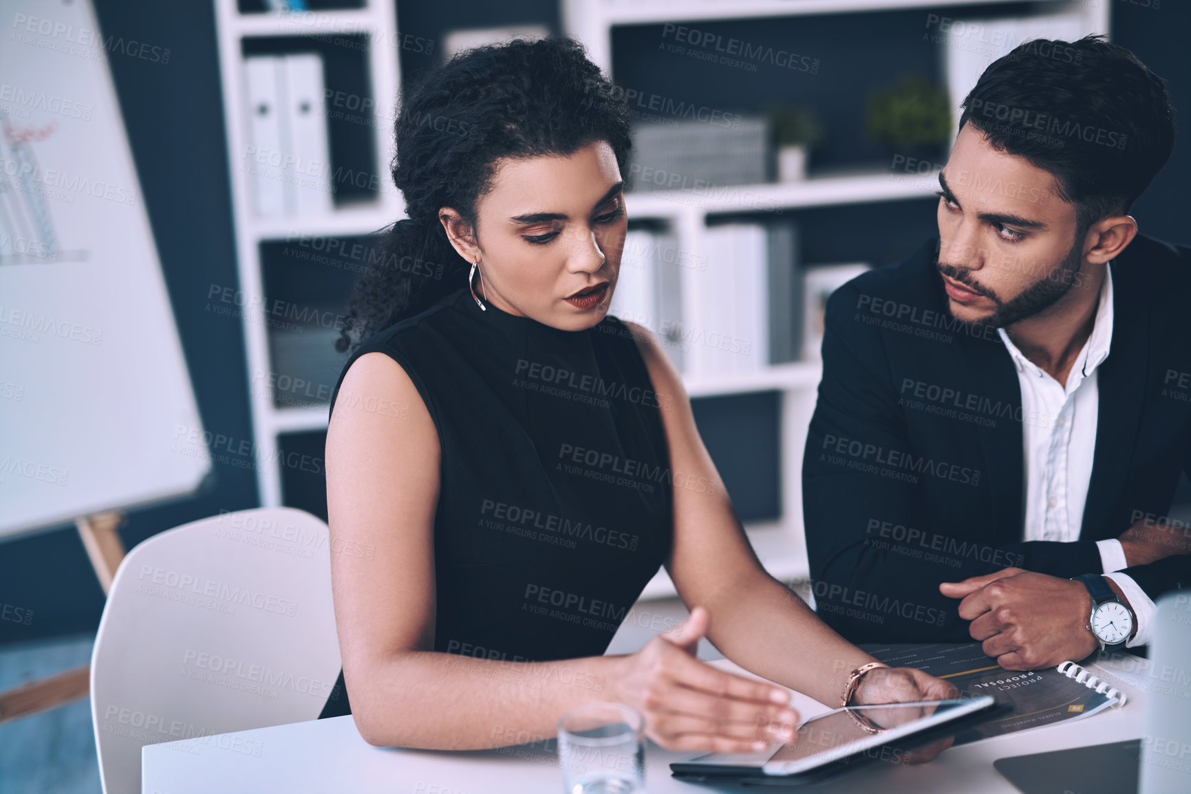 Buy stock photo Cropped shot of two young businesspeople sitting together and having a discussion while using a tablet in the office