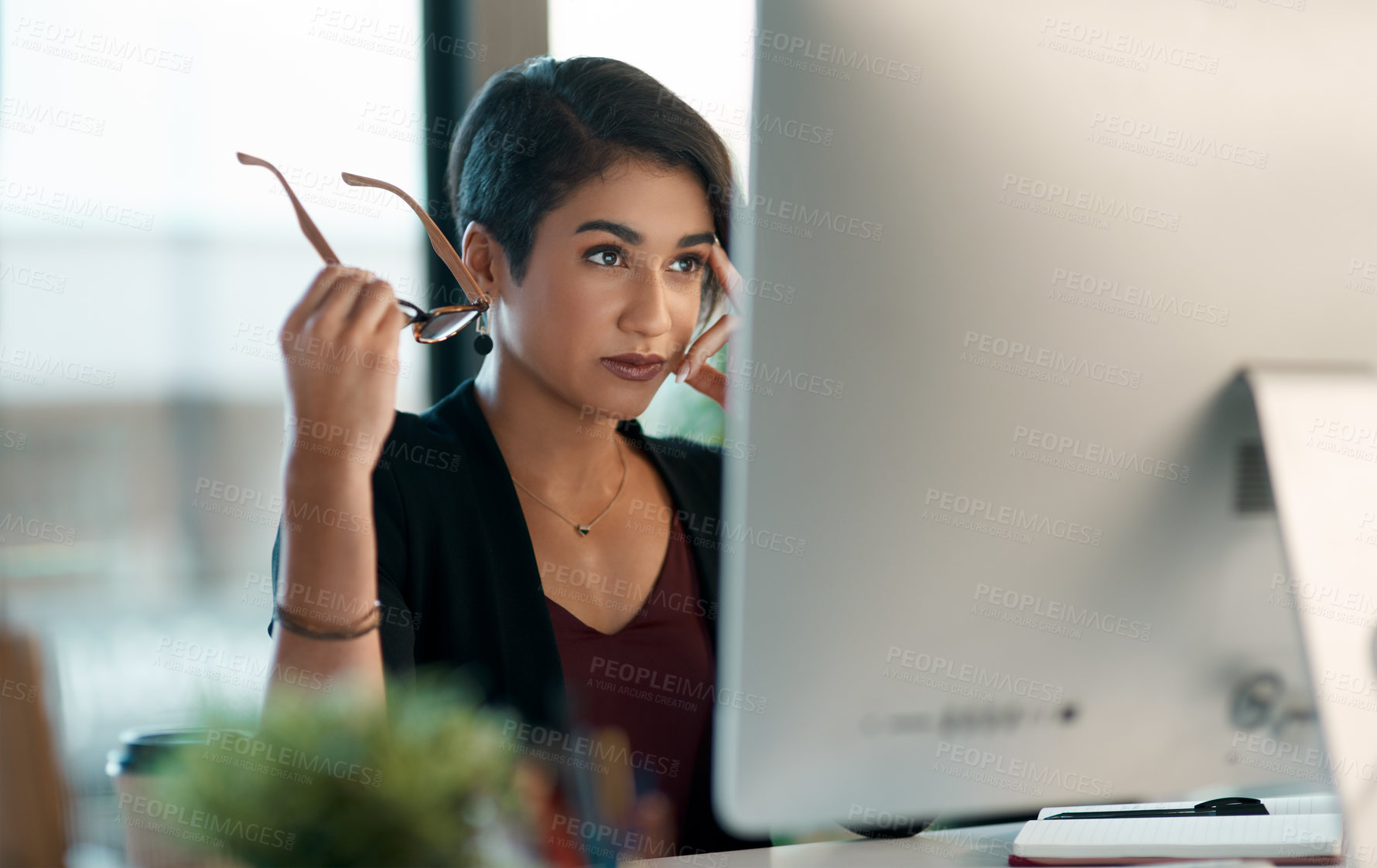 Buy stock photo Cropped shot of an attractive young businesswoman sitting alone and looking contemplative while working on her computer in the office