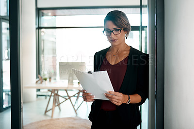 Buy stock photo Cropped shot of an attractive young businesswoman standing alone in her office and reading paperwork