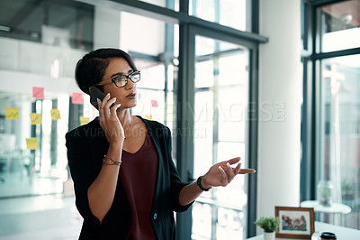 Buy stock photo Cropped shot of an attractive young businesswoman standing in her office alone and talking on her cellphone