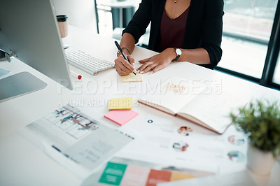Buy stock photo Cropped shot of an unrecognizable young businesswoman sitting in her office alone and writing in a notebook