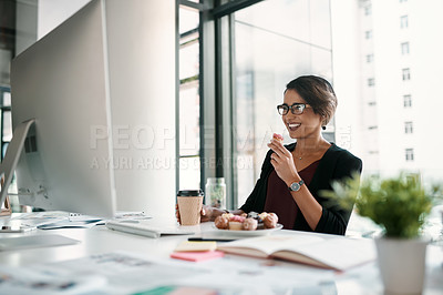 Buy stock photo Cropped shot of an attractive young businesswoman sitting alone at her desk and holding a cupcake