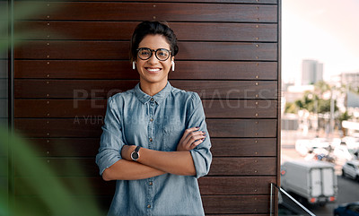 Buy stock photo Cropped portrait of an attractive young woman wearing earpods and standing on a balcony alone with her arms folded