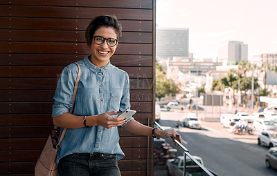 Buy stock photo Cropped portrait of an attractive young woman standing on a balcony alone and using her cellphone