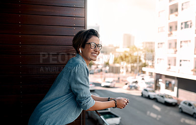 Buy stock photo Cropped shot of an attractive young woman wearing earpods and looking out into the city while standing on a balcony alone