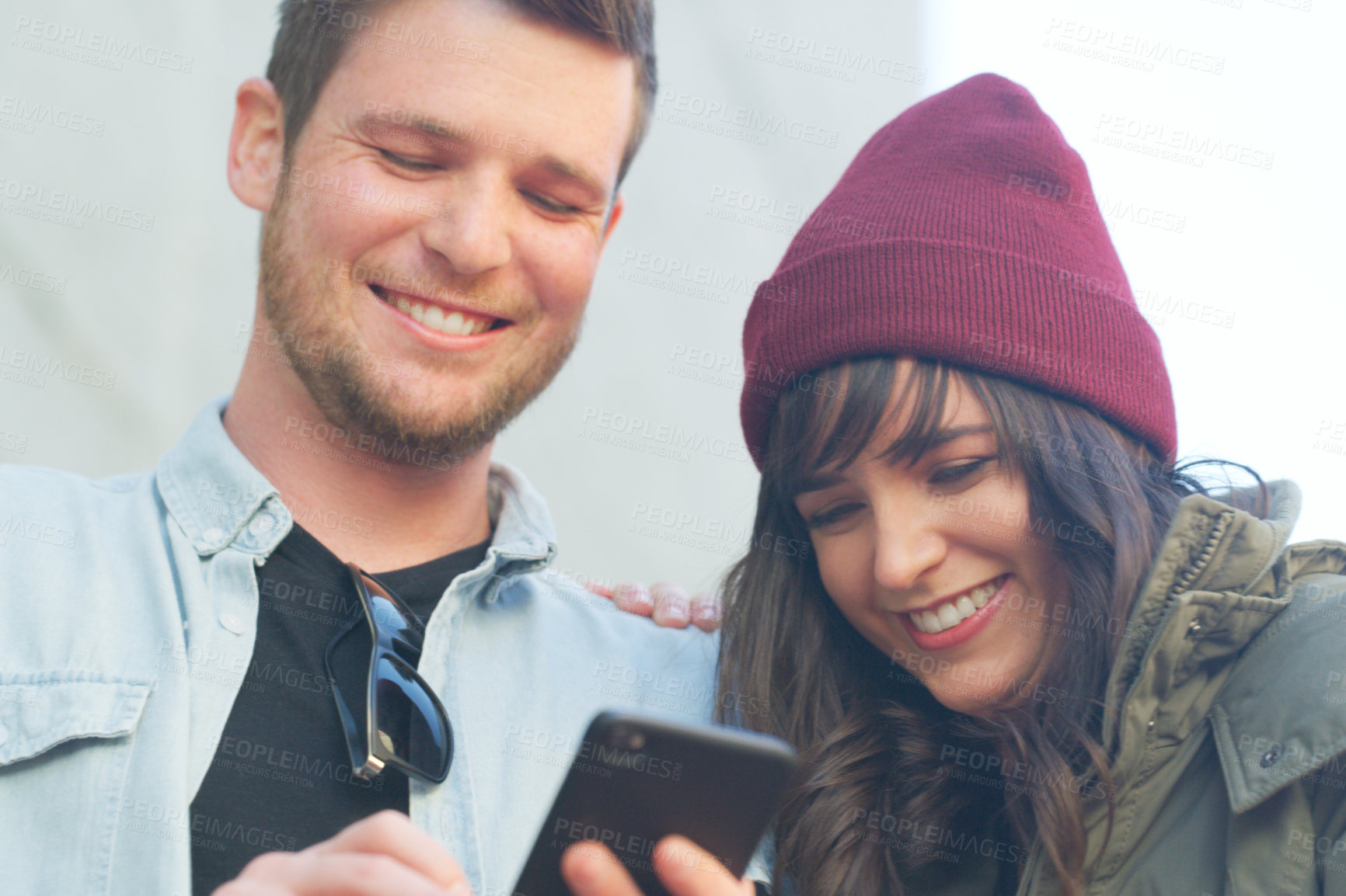 Buy stock photo Cropped shot of an affectionate young couple using a cellphone together outdoors