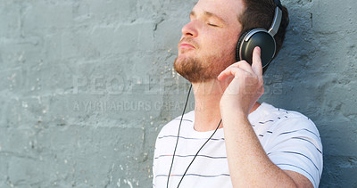 Buy stock photo Cropped shot of a handsome young man listening to music on his headphones outdoors