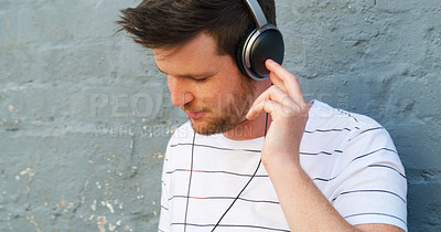 Buy stock photo Cropped shot of a handsome young man listening to music on his headphones outdoors