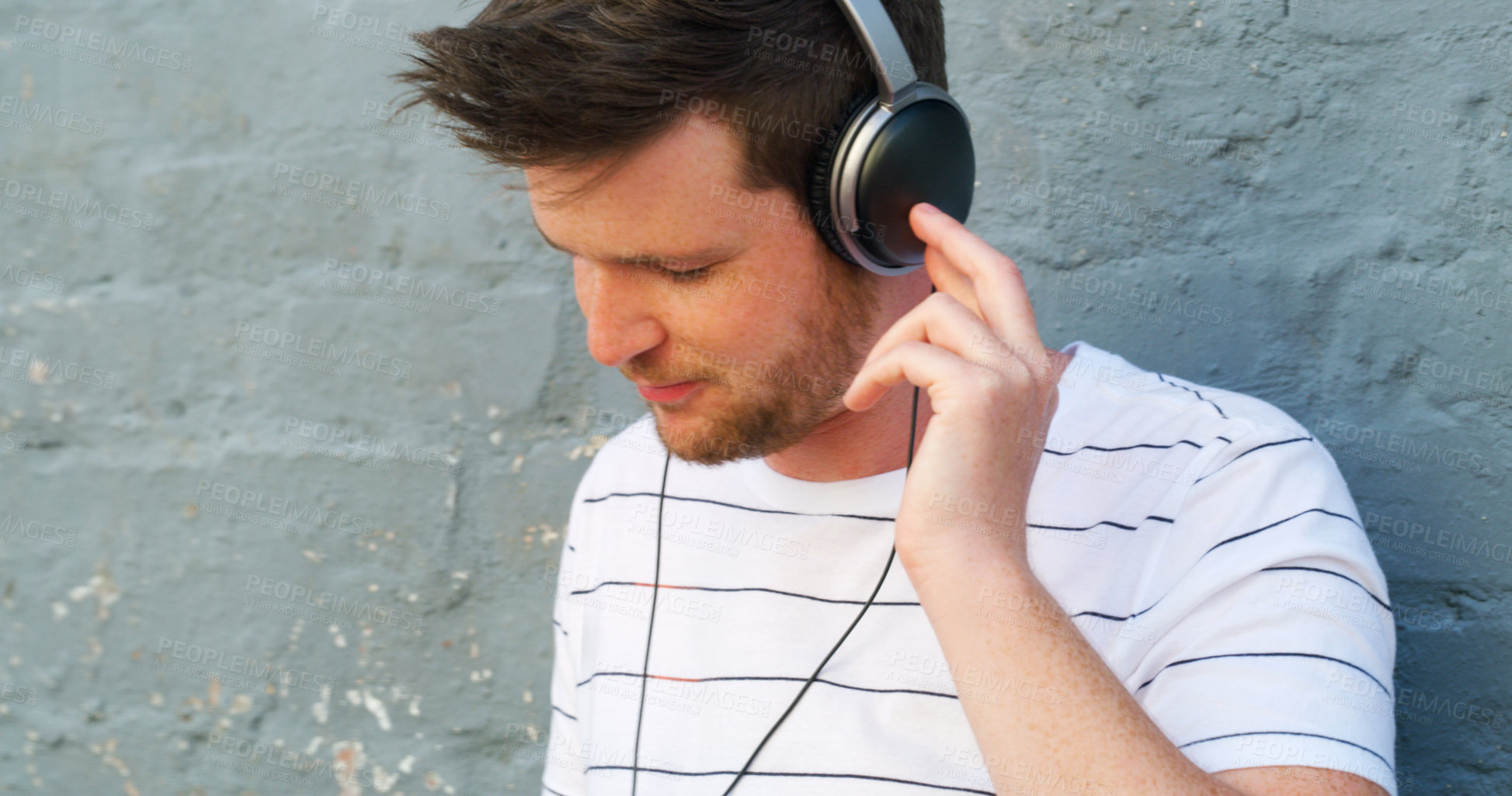 Buy stock photo Cropped shot of a handsome young man listening to music on his headphones outdoors
