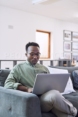 Buy stock photo Shot of a young businessman using a laptop on a sofa in a modern office