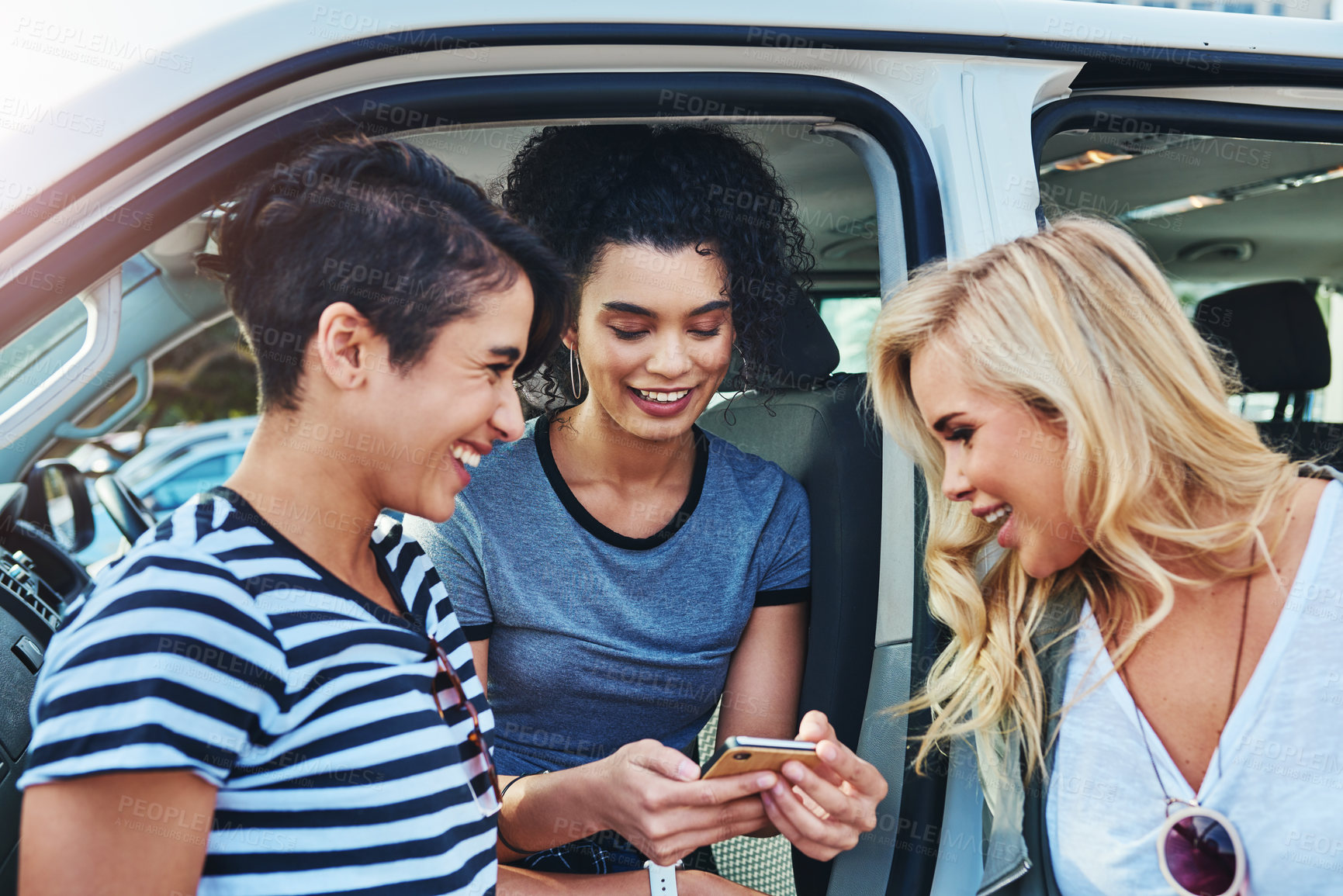 Buy stock photo Shot of friends looking at something on a cellphone while out on a road trip