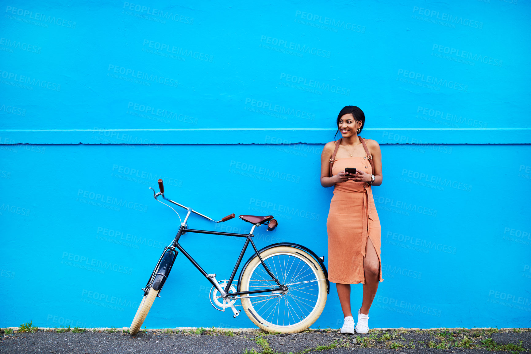 Buy stock photo Bicycle, young woman with smartphone and happy outside by blue wall. Cycling in urban area, health wellness and female person on cellphone outdoors standing in streets with bike or cycle in road