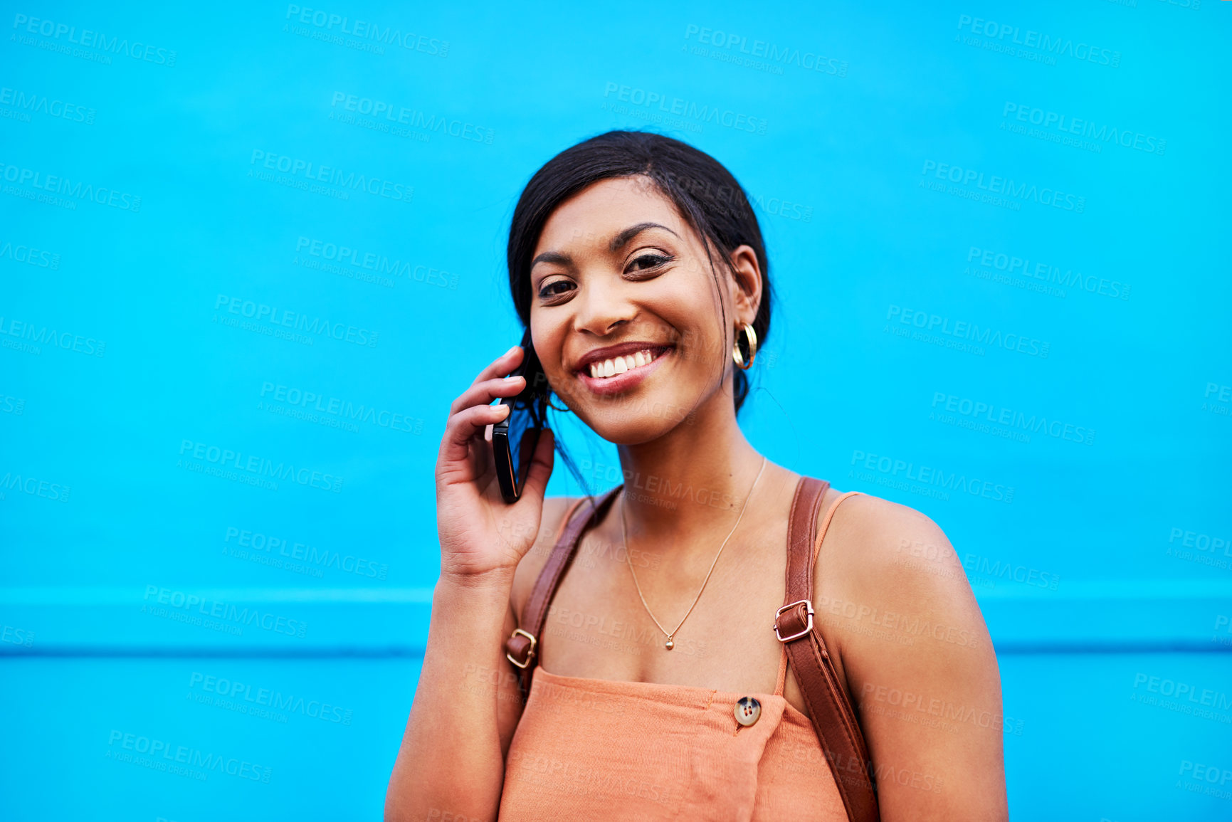 Buy stock photo Girl, portrait and happy with phone call outdoor for communication, conversation and backpack. Woman, student and talking on smartphone with consulting for university application on blue background