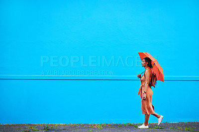 Buy stock photo Full length shot of an attractive young woman holding an umbrella while walking against a blue background outdoors