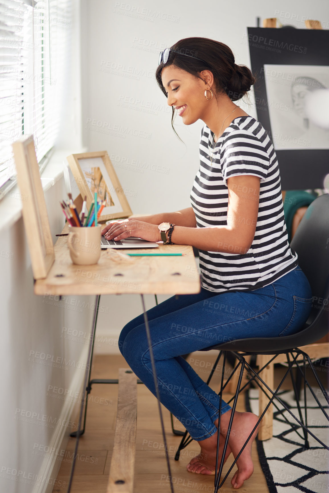 Buy stock photo Full length shot of an attractive and artistic young woman using a laptop while working inside her studio at home