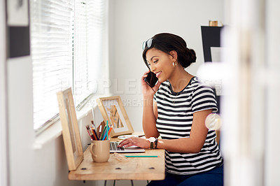 Buy stock photo Shot of an attractive young artist using a laptop and making a phone call inside her studio at home