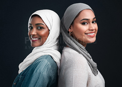 Buy stock photo Cropped shot of two attractive young women wearing hijabs and standing back to back against a black studio background