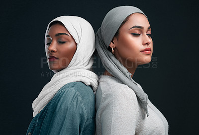 Buy stock photo Cropped shot of two attractive young women wearing hijabs and standing back to back against a black studio background