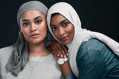 Buy stock photo Cropped shot of two attractive young women wearing hijabs and standing close together against a black background in the studio