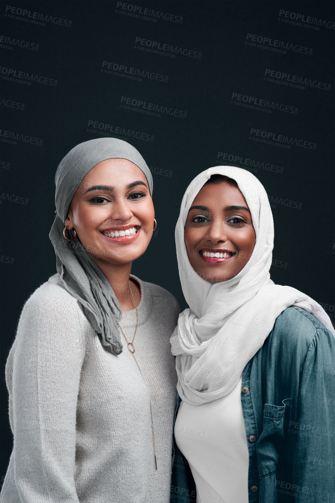 Buy stock photo Cropped shot of two attractive young women wearing hijabs and standing close together against a black background in the studio