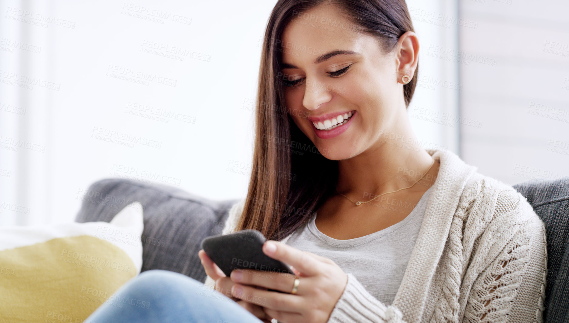 Buy stock photo Shot of an attractive young woman using her cellphone while relaxing on a couch at home