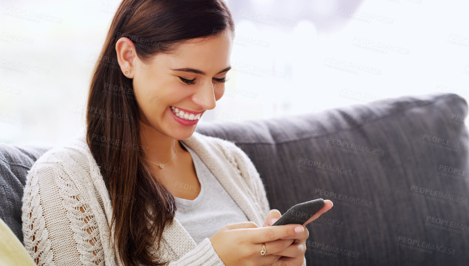 Buy stock photo Shot of an attractive young woman using her cellphone while relaxing on a couch at home