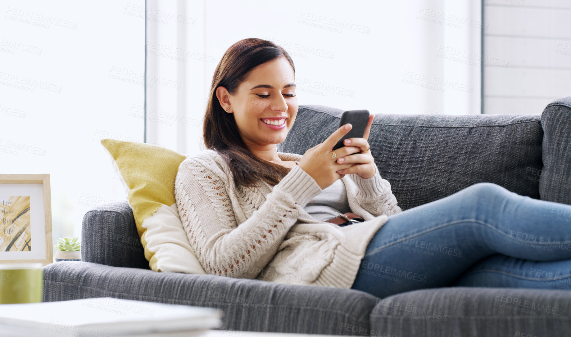 Buy stock photo Shot of an attractive young woman using her cellphone while relaxing on a couch at home