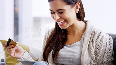 Buy stock photo Shot of an attractive young woman using her credit card and digital tablet while relaxing on a sofa at home