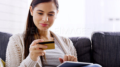 Buy stock photo Shot of an attractive young woman using her credit card and digital tablet while relaxing on a sofa at home