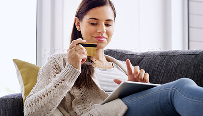 Buy stock photo Shot of an attractive young woman using her credit card and digital tablet while relaxing on a sofa at home