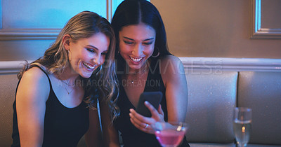 Buy stock photo Shot of two young women using a smartphone together in a nightclub