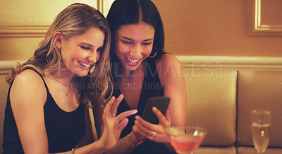 Buy stock photo Shot of two young women using a smartphone together in a nightclub