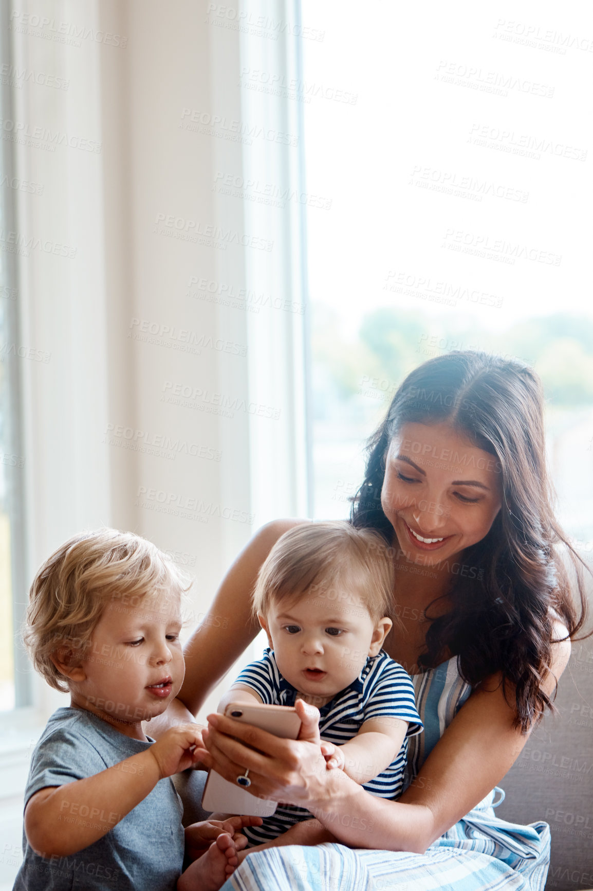 Buy stock photo Shot of a mother showing her tow little sons something on a cellphone at home