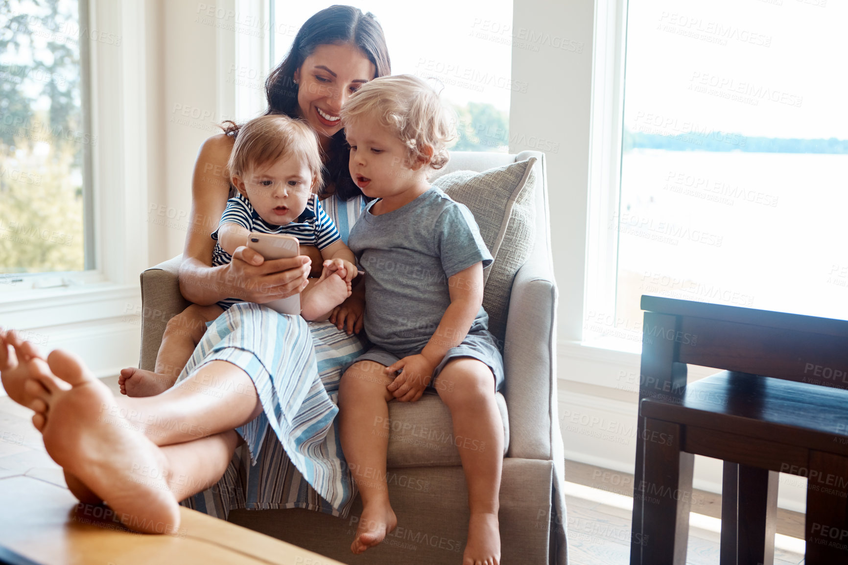 Buy stock photo Shot of a mother showing her tow little sons something on a cellphone at home