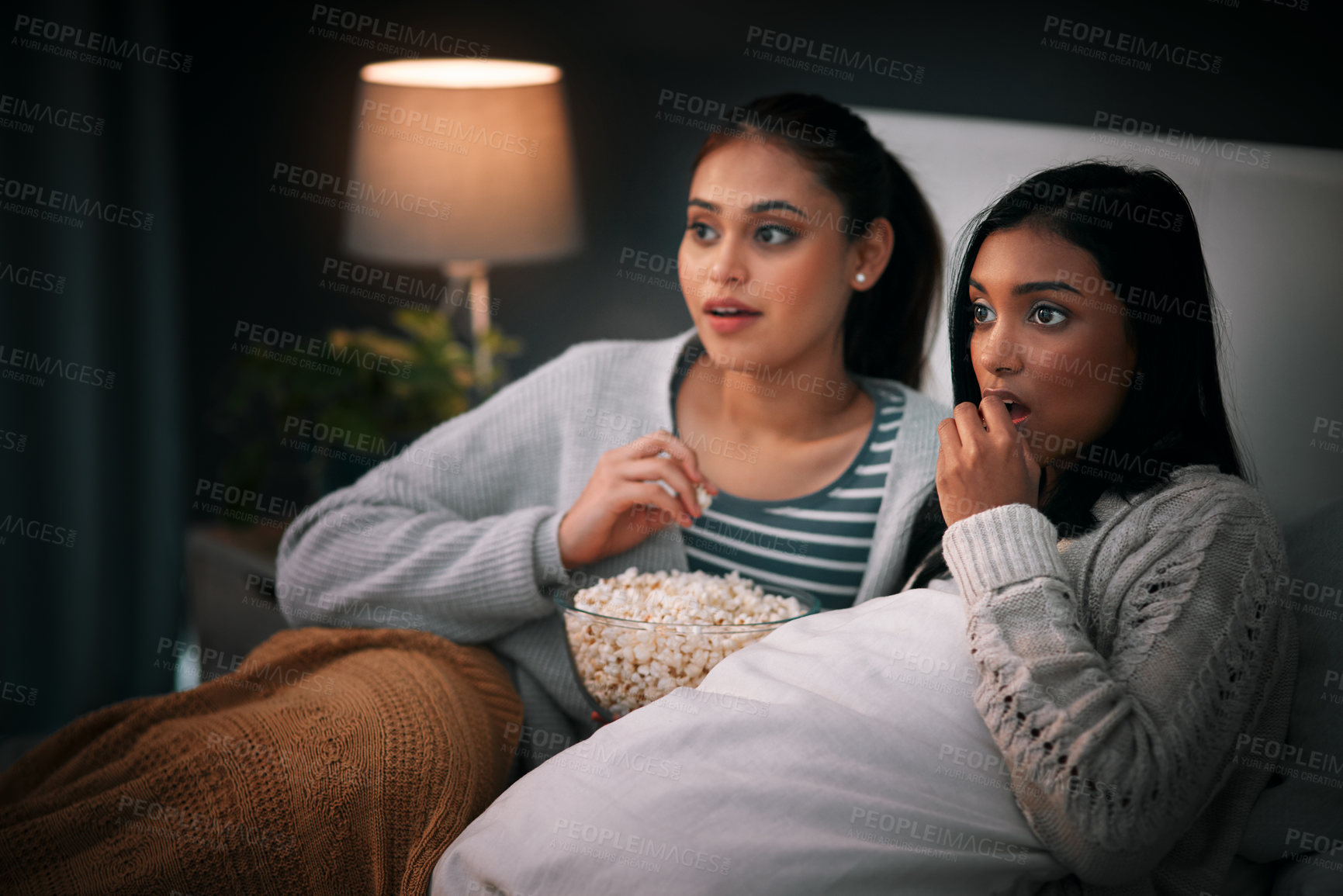 Buy stock photo Popcorn, eating and people or friends with horror movies, scary show and sleepover on bed, streaming service or television. Gen z women relax in bedroom for drama TV film, home cinema or subscription