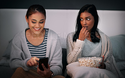 Buy stock photo Shot of a young woman looking displeased while her friend is browsing on her cellphone