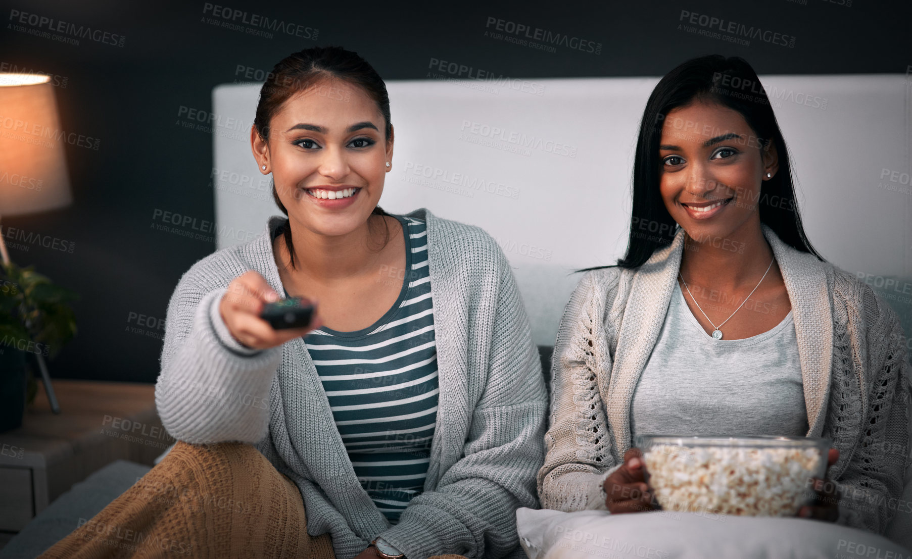 Buy stock photo Shot of two young women eating popcorn while watching a movie at home
