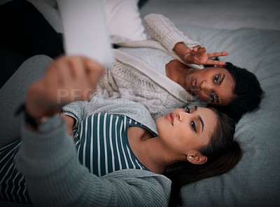 Buy stock photo Shot of two young women lying taking selfies while lying on a bed