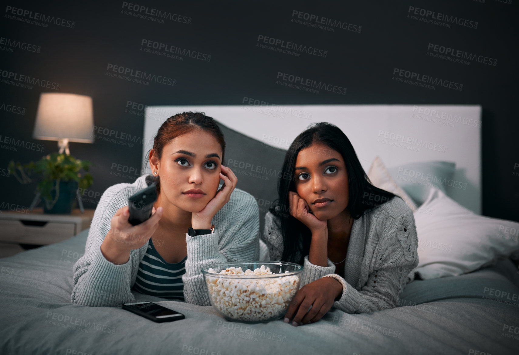 Buy stock photo Friends, women and watching tv in bed with popcorn for social visit, bonding and sleepover. People, relationship and home at night in bedroom for movie night, streaming series and entertainment