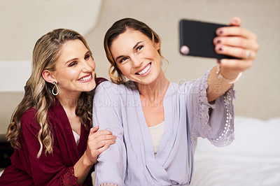 Buy stock photo Cropped shot of a beautiful young bride and her best friend taking a selfie together in their dressing room before the wedding