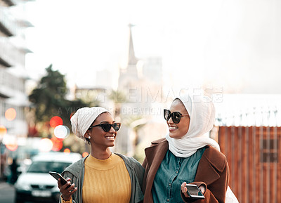 Buy stock photo Cropped shot of two attractive young muslim women wearing sunglasses and holding their cellphones while city sight-seeing
