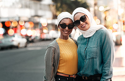 Buy stock photo Cropped shot of two attractive young women wearing sunglasses and headscarves while standing in the city