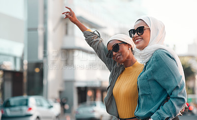Buy stock photo Cropped shot of two attractive young women wearing sunglasses and headscarves while hailing a taxi in the city