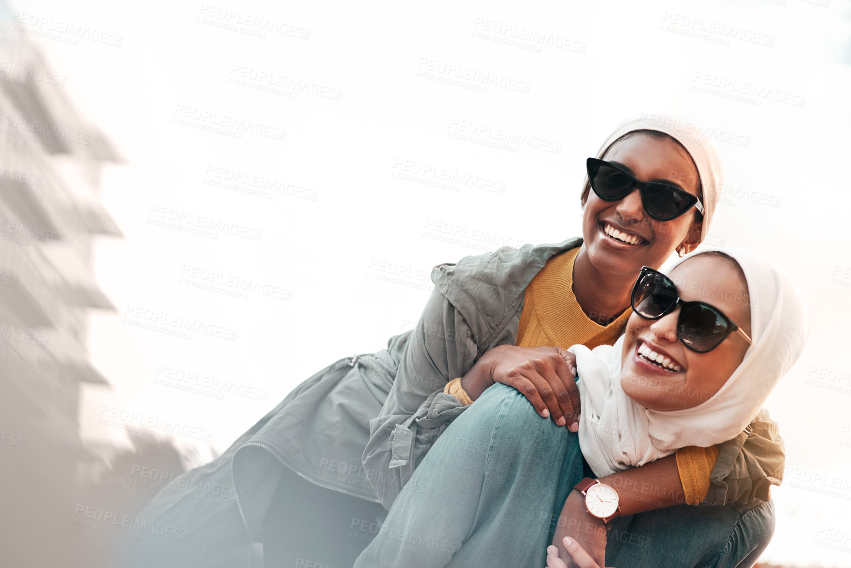 Buy stock photo Cropped shot of an attractive young woman wearing sunglasses and a headscarf while giving her female friend a piggyback ride
