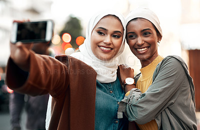 Buy stock photo Cropped shot of two attractive young women standing together and wearing headscarves while taking a selfie with their cellphone